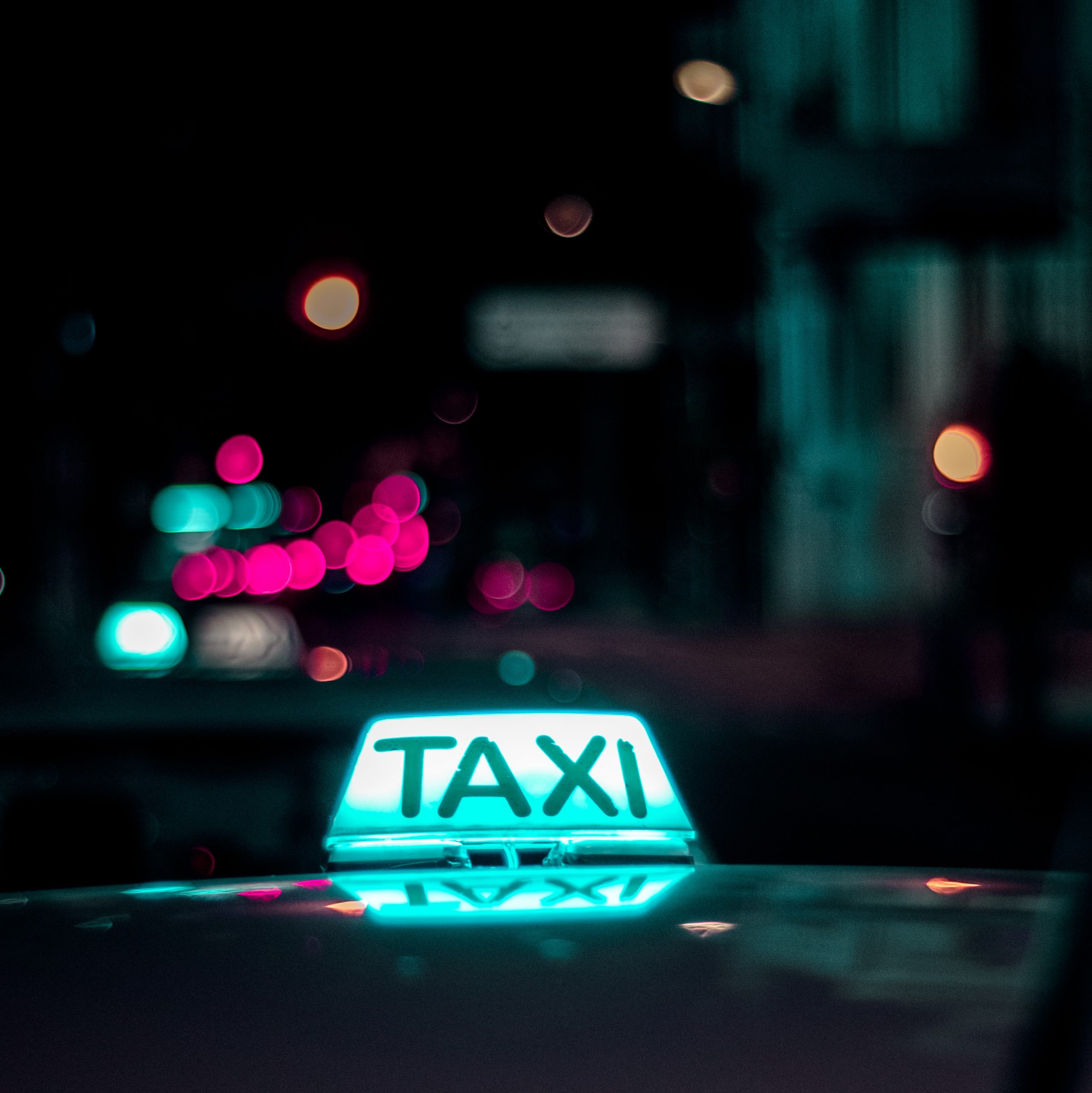 taxi cab sign lit up at night with blurry lights in background